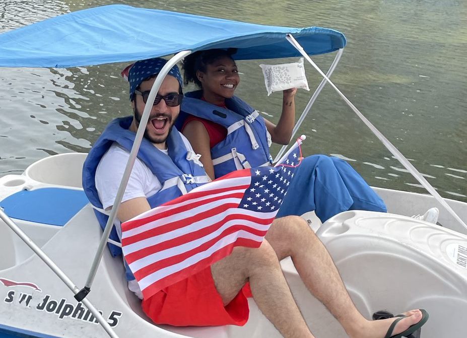 A photo of Twipes cofounders Al and Elle in a paddle boat holding up an American flag and a pack of Twipes to celebrate the company's expansion to America.