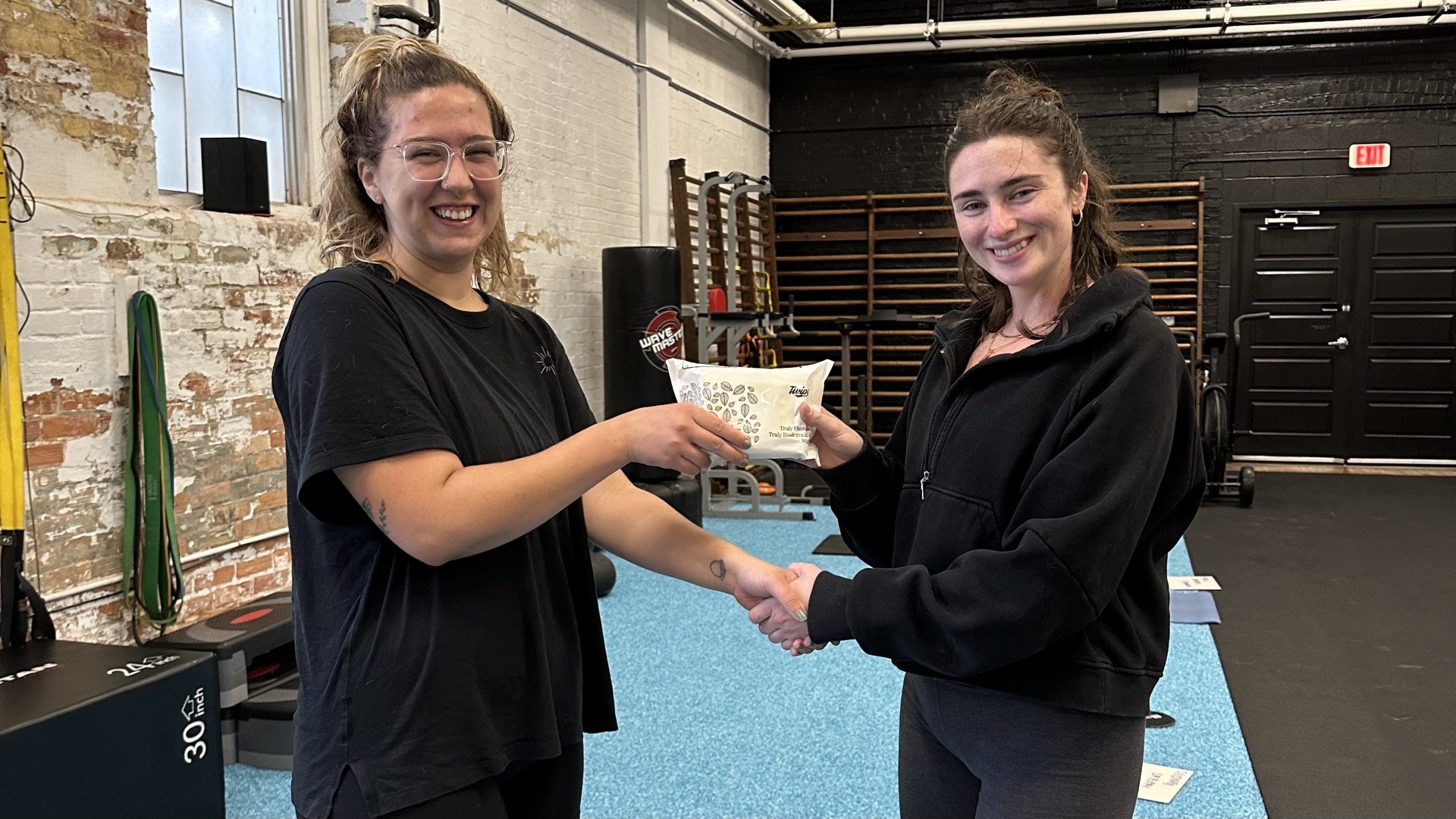 A photo of two women from Evolve Fitness posing with a pack of Twipes